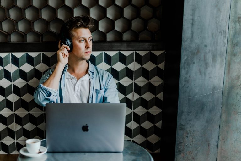 a male employee listening to recordings on his headphones in front of his laptop and coffee before transcribing